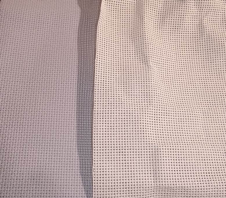 Picture of 2 different types of Aida cross stitch fabric. The one on the left is 14 count light gray fabric, the one on the right is also 14 count but in an off-white/ivory/ecru color and the holes are ridiculously huge.