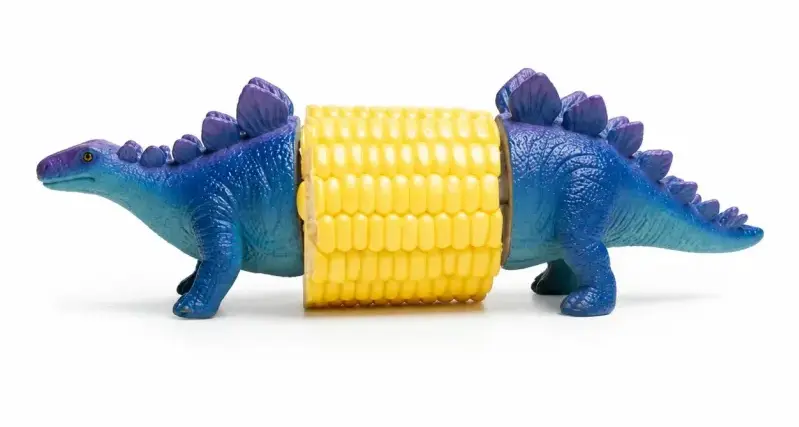 a small ear of corn with corn holders at either end that look like the front and back end of a stegosaurus in shades of purple at the back plates and gradiating down to light blue on the underbelly and legs.
