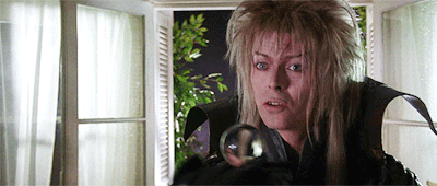 Looping gif of David Bowie as the Goblin King in Labyrinth doing some one-handed contact juggling with a clear ball.