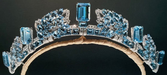 Aquamarine and diamond tiara featuring alternating motifs of pinecones made from clusters of pear-shaped aquamarines and rectangular aquamarines set in platinum with verticle bands of diamonds where they meet the band. The base features a band of small, rectangular aquamarines on their long side, above which is a band of diamonds. The frame is wrapped in very light brown velvet.