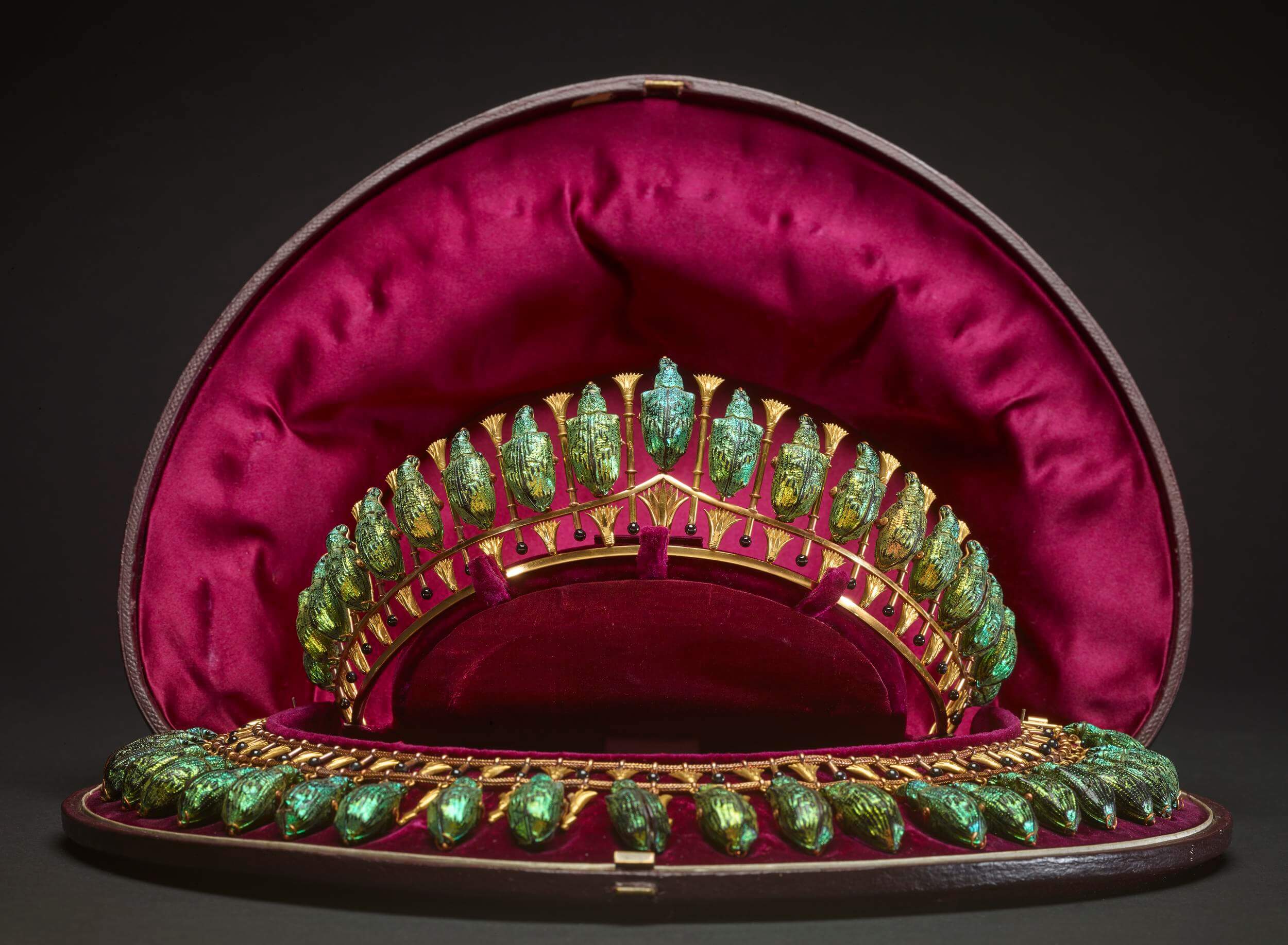 Tiara and necklace set with iridescent weevil shells. In between the weevils are tiny gold rods with a black enamel bead on the bottom and a lotus motif on the top. They are in a leather-covered case lined with red silk.