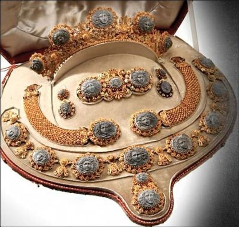A set of jewelry in a velvet-lined case. The set is made of gold with cameos in the shape of Medusa heads carved out of lava rock. There is a tiara, brooch, two bracelets, earrings and necklace.