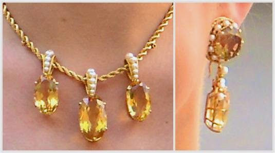 Left: Gold, citrine and seed pearl necklace. The chain is a thick twisted gold rope. There are 3 necklace pendants or slides, each one an oval citrine with the center one being slightly larger. The bale (or loop) is a single row of seed pearls. Right: One of the earrings from the parure features a large round gem circled with seed pearls with a large citrine drop.