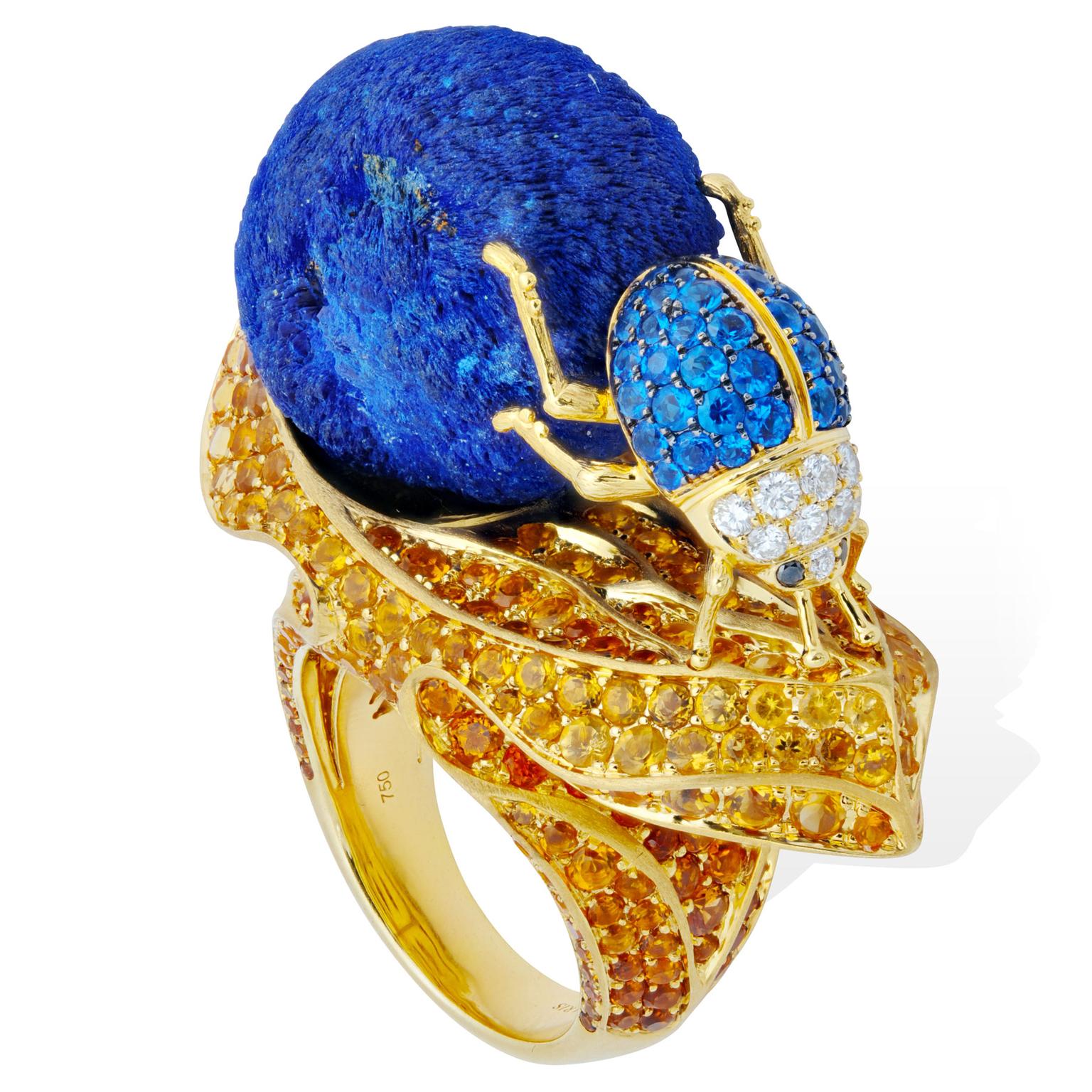 Golden ring featuring a dung beetle pushing a ball of dung which is actually azurite. The ring is studded with haüynites, topazolites, hessonites, white diamonds and brown diamonds.