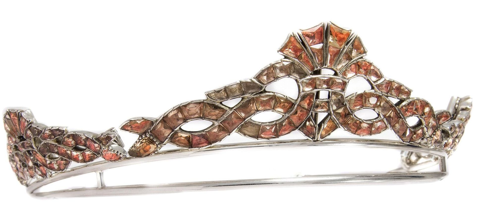 Silver tiara set with topazes. Three large silver bows of interwoven ribbons are set atop a simple semi-circular base. The silver is set with Imperial topaz gemstones backed with foil to increase their shine. The hues of the stones range from a vivid orange-red to a more delicate rose shade.
