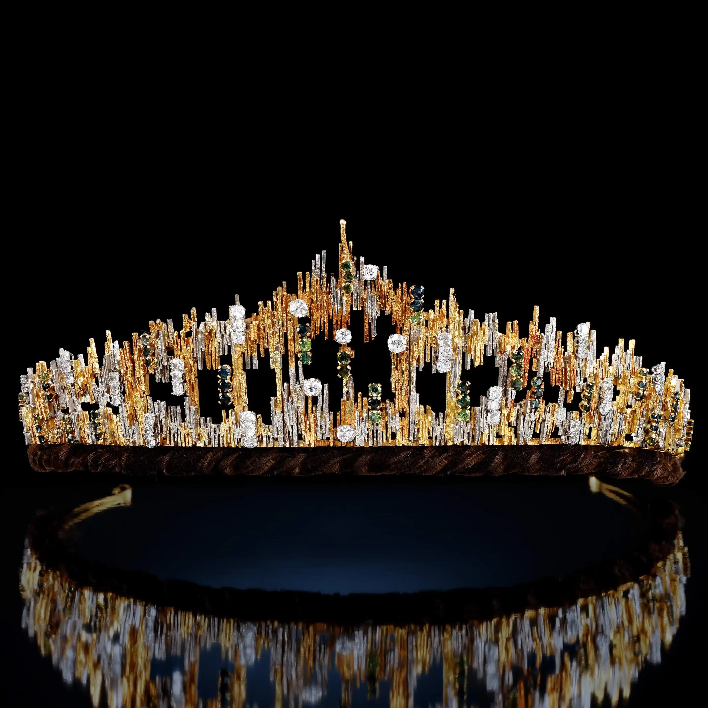 Gold tiara in gold and silver spiky design, with a bottom band and a small arch that comes to a point. The tiara is studded with brilliant- and circular-cut diamonds and circular-cut green tourmalines.