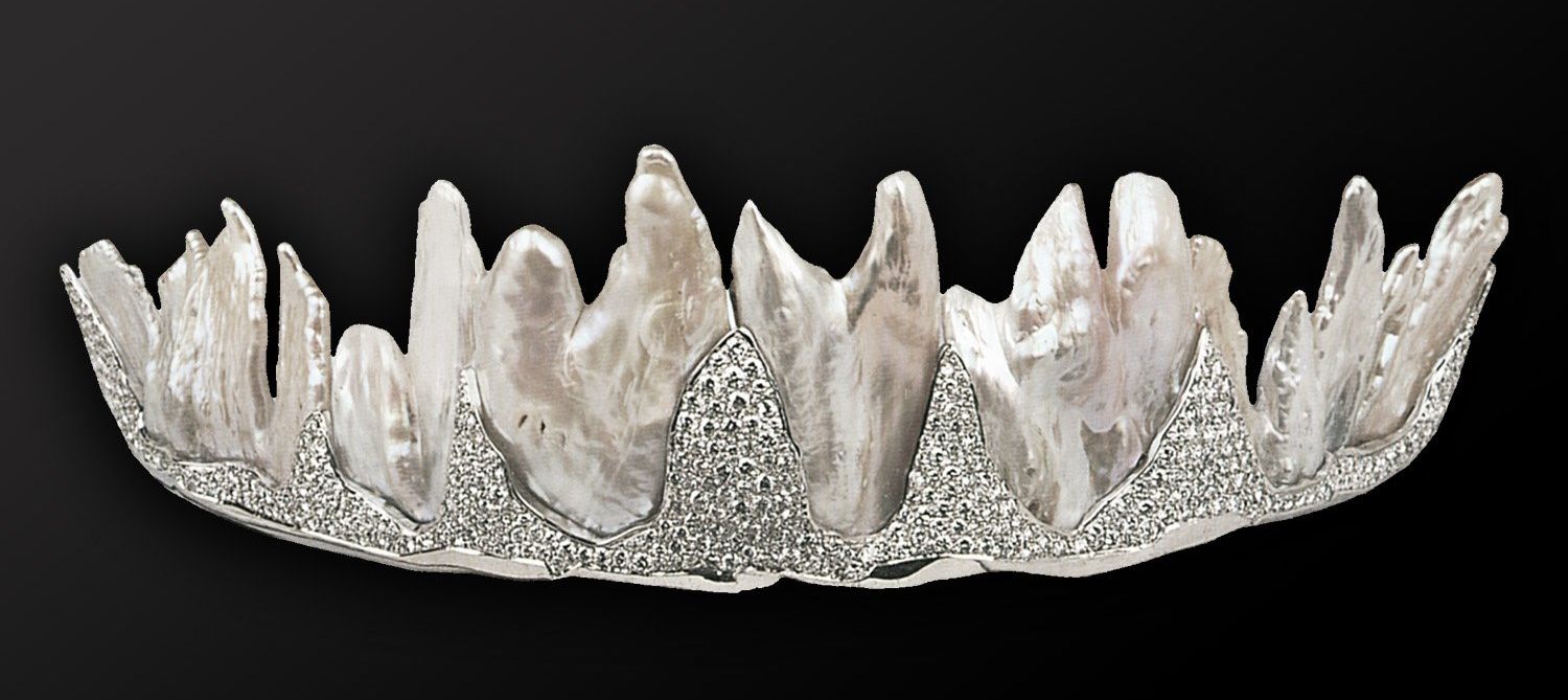 The Fire and Ice Tiara is created from cultured freshwater baroque pearls, white gold and diamonds. The front portion of the tiara is a ring of jagged white gold peaks covered in small diamonds. Behind this row is a taller row of 6 irregularly-shaped baroque pearls.