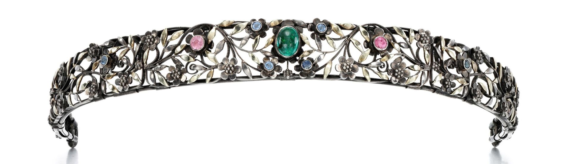 Silver openwork bandeau style tiara with small flowers and leaves. In the center is an oval cabochon emerald. Several of the larger flower elements on the bandeau are set with blue or pink round sapphires.
