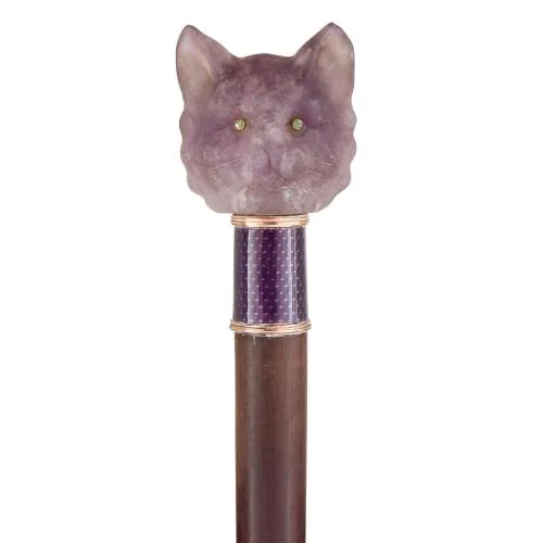 Walking stick with a carved amethyst cat head topper with green demantoid garnet eyes. The band joining the head to the cane is guilloché enamelled with gold rings at top and bottom, a purple background, and gold wavy motif. The cane is a deep brown hardwood.