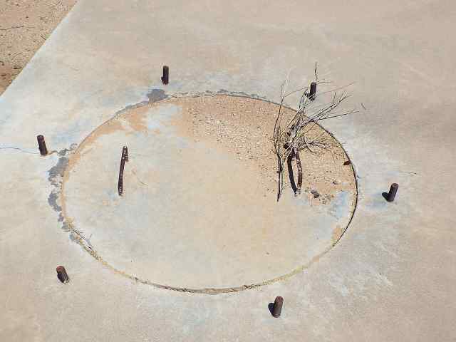 closeup photo of a manhole with cement cover with rebar handles on one of the calibration crosses. Around the cover are 6 equally spaced pieces of rebar sticking up.