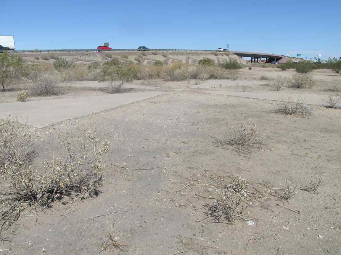 photo of a large concrete cross in a dirt area just off a freeway overpass that is in the background.