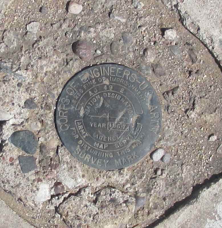 photo of a metal survey marker with these words printed on it: CORPS OF ENGINEERS US ARMY SURVEY MARK - $250 fine or imprisonment for disturbing this marker - AJ 49 2 STATION DESIGNATION YEAR 1967 AGENCY ARMY MAP SERVICES